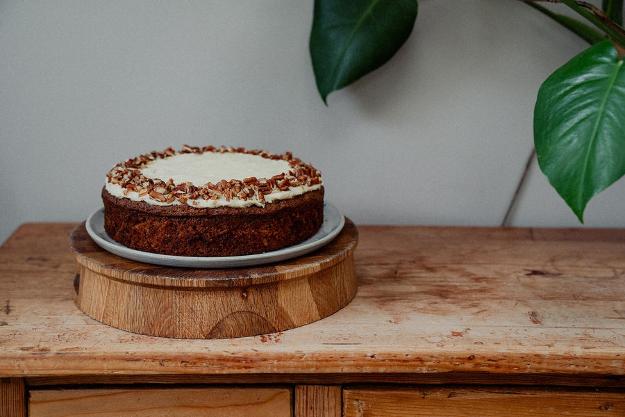 Carrot cake with white frosting on a wooden stand with a plant in the background